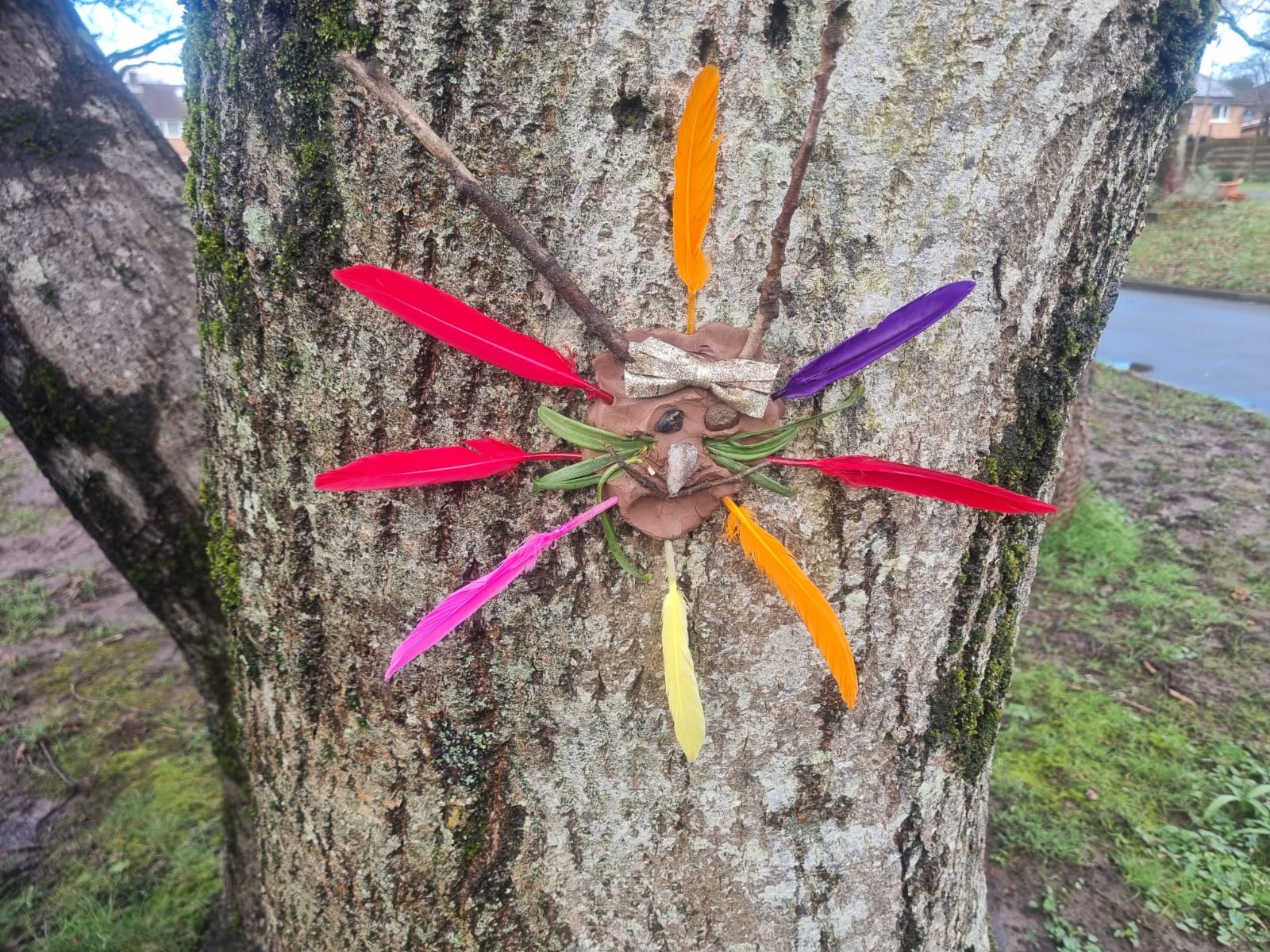 Clay face on a tree with coloured feathers for hair